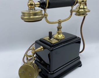 Pode incluir: Um telefone preto antigo com detalhes em latão. O telefone possui um fone, um receptor e um mostrador. A base é retangular e o telefone tem um fio. O telefone é um item vintage.