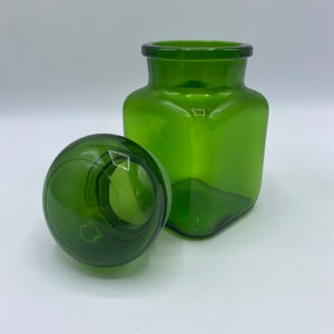 May include: A green glass jar with a matching lid. The jar has a square shape and the lid is round.