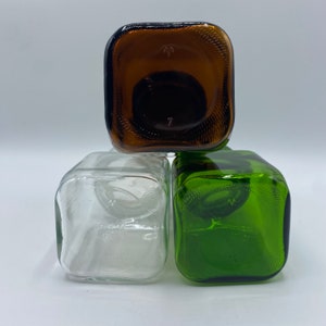 May include: Three square glass bottles, one brown, one clear, and one green, stacked on top of each other.
