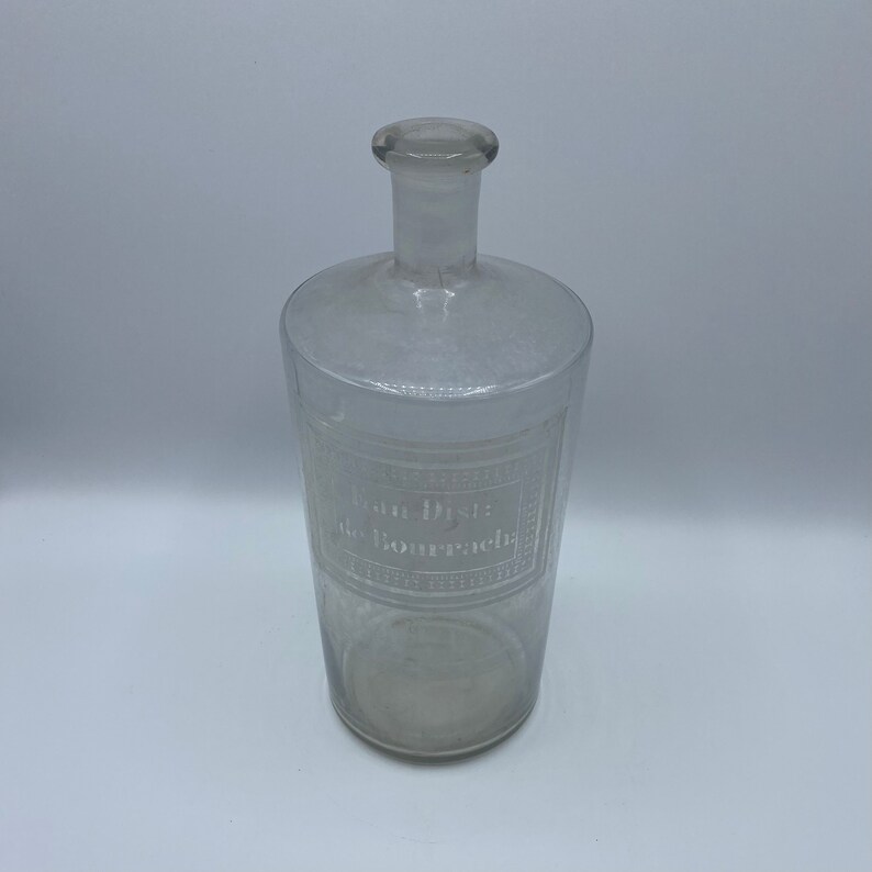 May include: A clear glass bottle with a textured surface and a label that reads "Eau Distillee de Bourrache".