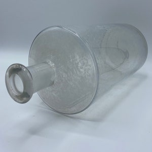 May include: A clear glass bottle with a textured surface and a round opening at the top.