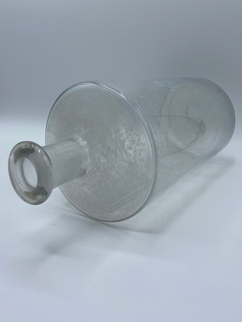 May include: A clear glass bottle with a textured surface and a round opening at the top.