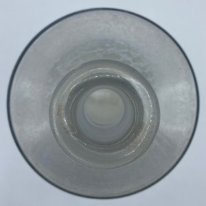 May include: A clear glass bottle with a wide mouth and a smooth, rounded bottom. The bottle is empty and has a slight frosted appearance.