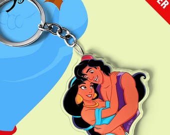 May include: A clear acrylic keychain featuring a colorful illustration of a man and a woman embracing. The keychain is attached to a silver metal split ring. The background graphic shows a blue genie and text reading Carlos Gromo and PRE-ORDER.
