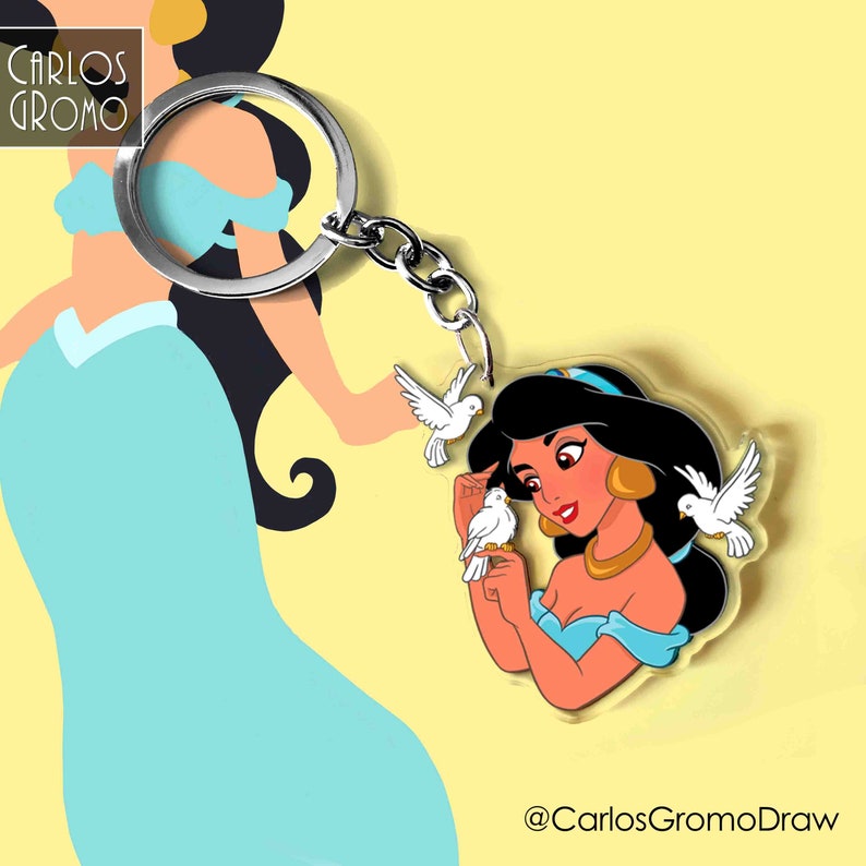 K&ouml;nnte beinhalten: Ein durchsichtiger Acryl-Schl&uuml;sselanh&auml;nger mit einer Cartoon-Illustration von Prinzessin Jasmin aus Disneys Aladdin. Jasmin tr&auml;gt ein blaues und goldenes Outfit und h&auml;lt zwei wei&szlig;e Tauben. Der Schl&uuml;sselanh&auml;nger ist an einem silbernen Schl&uuml;sselring befestigt.