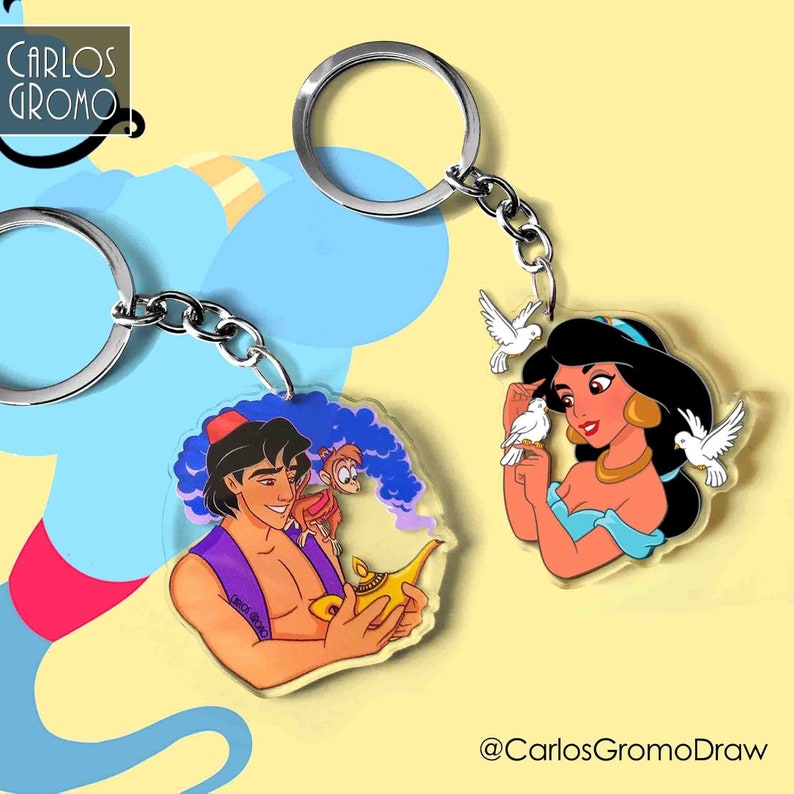 K&ouml;nnte beinhalten: Ein Set mit zwei Schl&uuml;sselanh&auml;ngern mit Figuren aus dem Disney-Film Aladdin. Ein Schl&uuml;sselanh&auml;nger zeigt Aladdin mit einer Genielampe und Abu dem Affen. Der andere Schl&uuml;sselanh&auml;nger zeigt Jasmin mit zwei wei&szlig;en Tauben. Die Schl&uuml;sselanh&auml;nger sind aus klarem Acryl und haben eine silberne Kette.