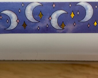 May include: A blue and white washi tape with a repeating pattern of gold crescent moons and stars.