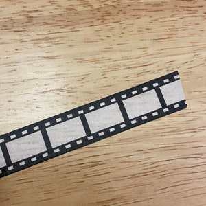 May include: A black and white film strip with a white background. The film strip is on a wooden surface.