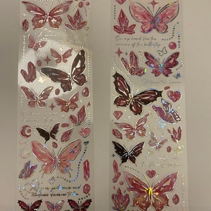 May include: Two sheets of pink and silver holographic stickers featuring butterflies, crystals, and inspirational quotes. The quotes are "On my hand lies the remains of the butterfly" and "A couple of wings quiver slightly with kindness."