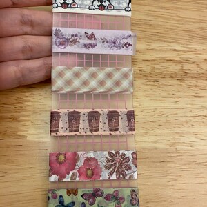 May include: A set of six decorative washi tapes featuring various designs, including a row of cartoon dogs peeking over a white border, a floral pattern with purple flowers and butterflies, a plaid pattern with beige and brown squares, a pattern of brown coffee cups with white polka dots, a floral pattern with pink flowers and leaves, and a pattern of green butterflies on a light green background.