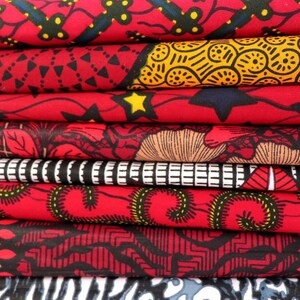 May include: A stack of eight red, black, and yellow patterned fabric swatches. The fabric has a variety of geometric and floral designs.