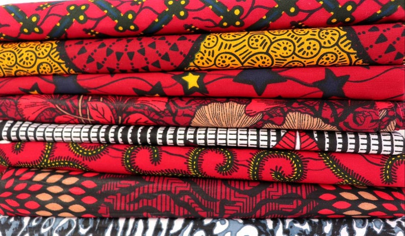 May include: A stack of eight red, black, and yellow patterned fabric swatches. The fabric has a variety of geometric and floral designs.