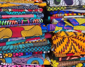 May include: A stack of colorful fabric with various patterns, including geometric, floral, and abstract designs. The fabric is folded neatly and arranged in a vertical stack.