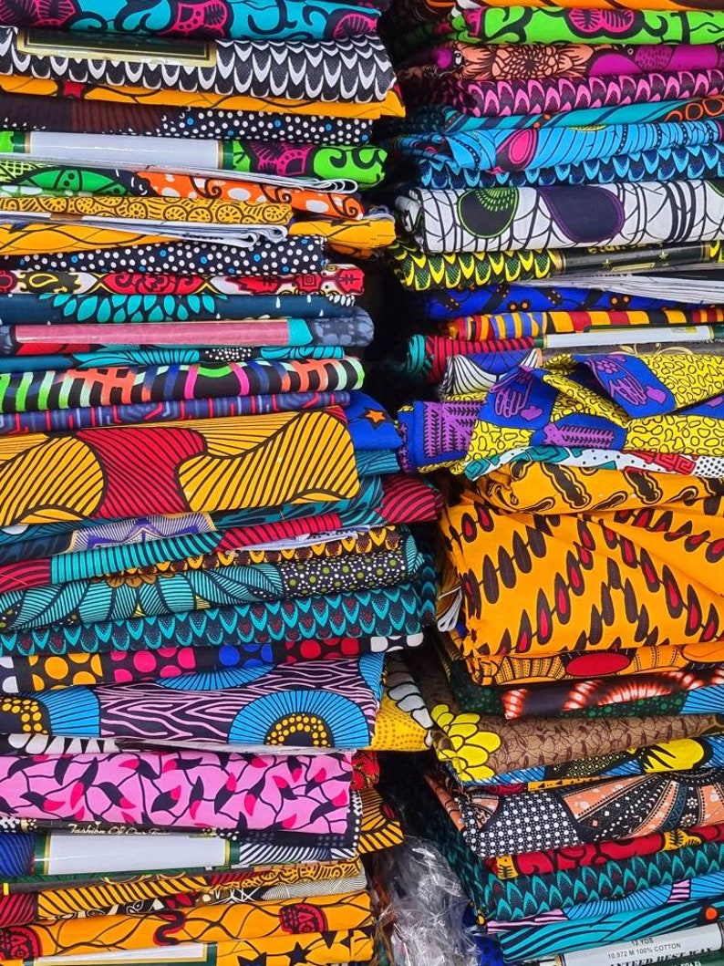 May include: A stack of colorful fabric with various patterns, including geometric, floral, and abstract designs. The fabric is folded neatly and arranged in a vertical stack.