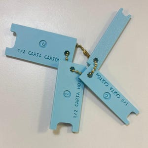 May include: Light blue cardstock paper pieces connected by a gold chain. Each piece has the text "1/2 CARTA CARTON" or "1/4 CARTA CARTON" printed on it. The pieces have a unique shape with a curved top and a notch at the bottom.