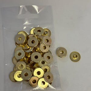 May include: A bag of gold-colored metal rings with a hole in the center. The rings are in a clear plastic bag and there are two rings outside of the bag.