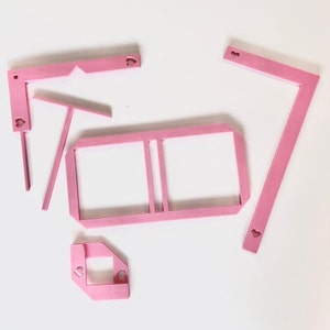 May include: Five pink plastic pieces with heart cutouts. The pieces are various shapes and sizes, including a rectangle, a square, and two L-shaped pieces.