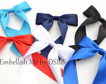 May include: Six satin ribbon bows in various colors, including turquoise, navy blue, black, white, red, and royal blue. The bows are tied with long tails and are arranged on a white surface. The text "Embellish Me by OSBB" is visible in the lower left corner of the image.