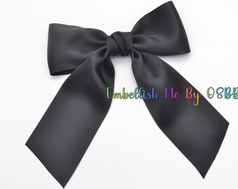 May include: A large black satin bow with long tails. The bow is tied in a center knot and the tails are flowing down.