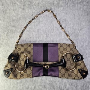 Könnte beinhalten: Eine braune und beige Gucci Handtasche mit einem violetten und schwarzen gestreiften Stoffpanel. Die Tasche hat einen goldenen Kettenriemen und einen goldenen Pferdekopfverschluss.