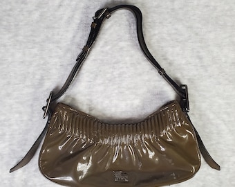 Könnte beinhalten: Eine braune Ledertasche mit einem schwarzen Riemen und einem Burberry-Logo. Die Tasche hat ein plissiertes Design und eine glänzende Oberfläche.