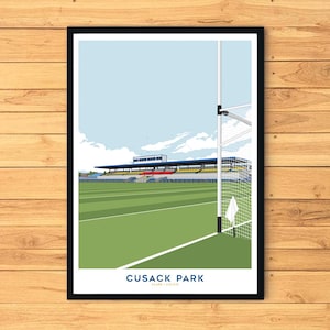 Op de afbeelding: Een ingelijste print van Cusack Park, een sportstadion. De afbeelding toont een groen veld, tribunes en een doelpaal tegen een blauwe lucht. De tekst "CUSACK PARK" staat onderaan.