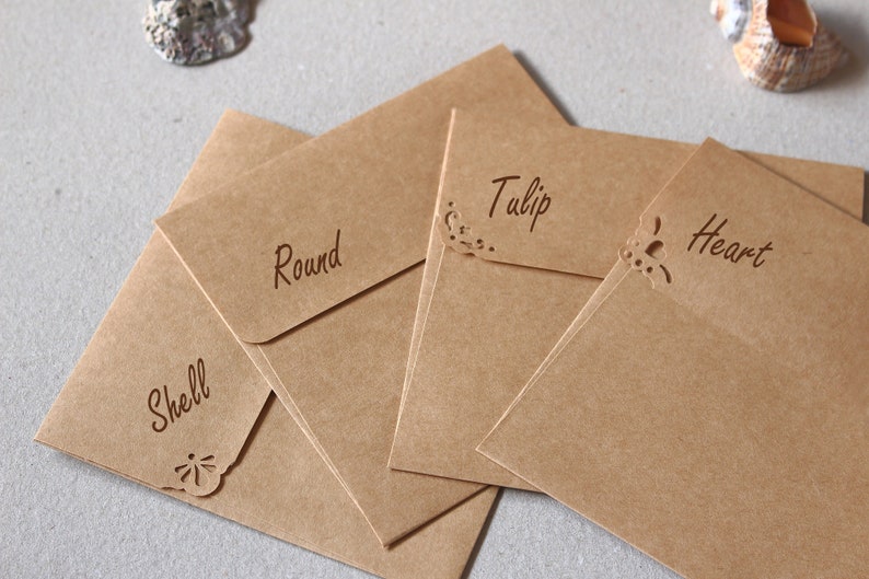 May include: Kraft paper envelopes with decorative cut-out corners. Each envelope is labelled with a word: Shell, Round, Tulip, and Heart. The envelopes are arranged in a slightly overlapping pattern.