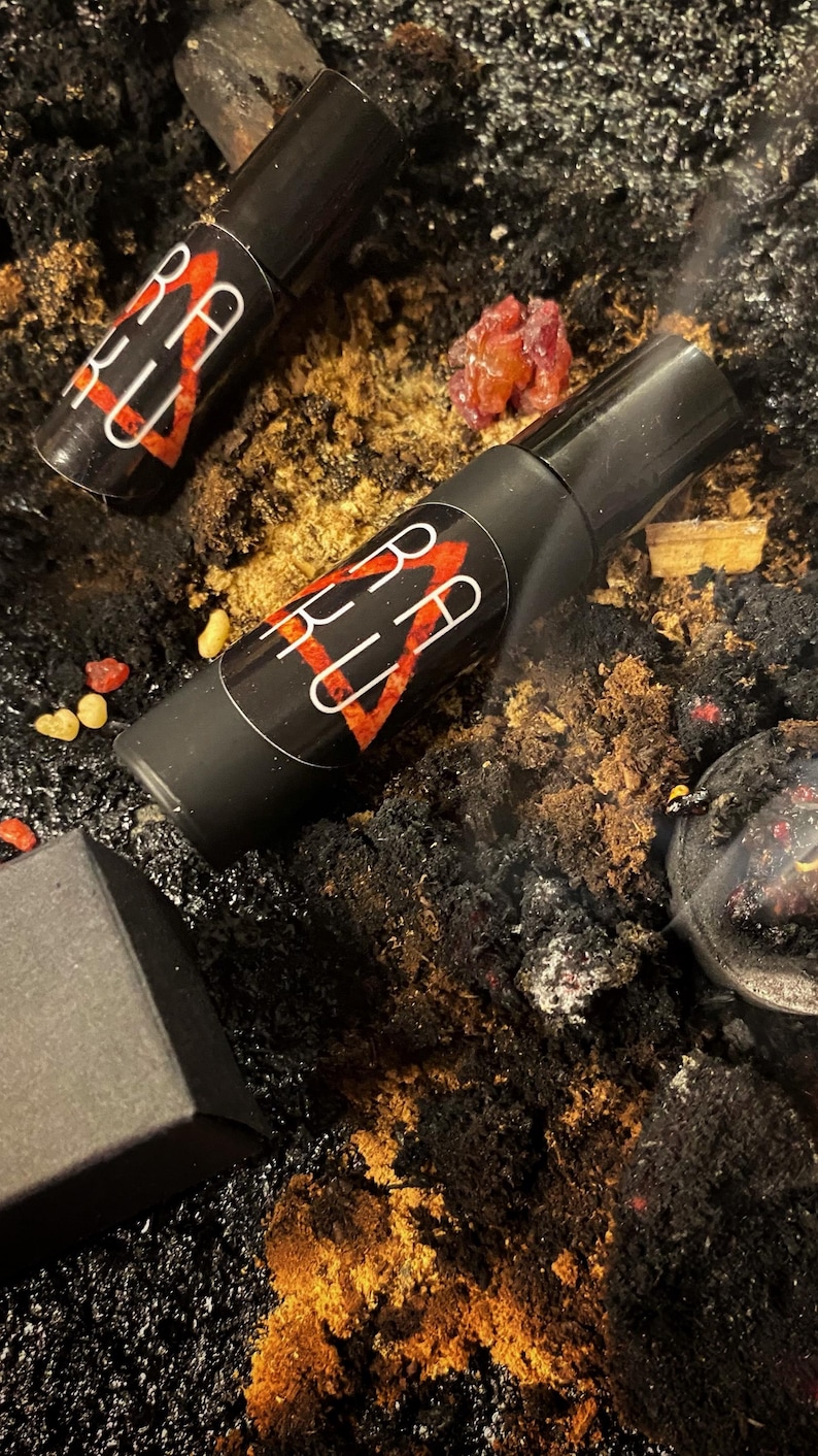 May include: Two black roller bottles with red and white labels that say "BELLU" on a dark background with orange and red pieces of resin.