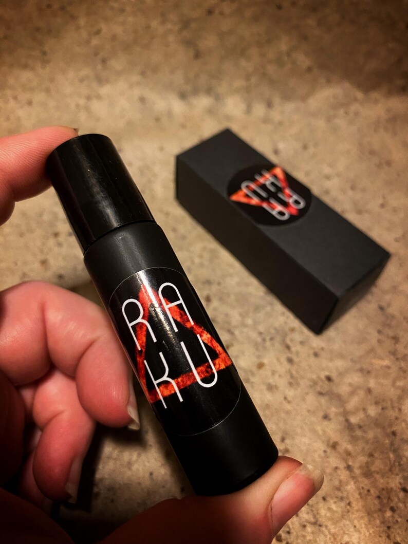 May include: A black roller bottle with a red and white triangle logo that says "RAKU" inside the triangle. The bottle is being held by a hand.