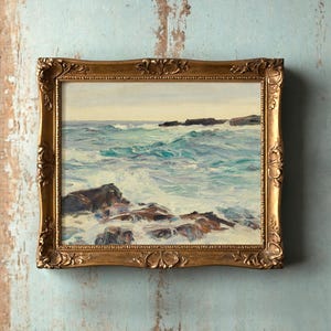 A framed painting of a seaside scene on a rustic turquoise wall. Rough waves crash against rocks, conveying a sense of movement and tranquility.
