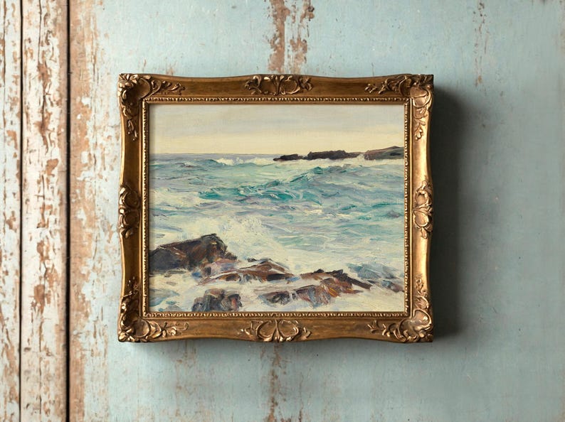A framed painting of a seaside scene on a rustic turquoise wall. Rough waves crash against rocks, conveying a sense of movement and tranquility.