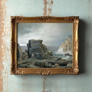A painting in an ornate gold frame shows a rugged coastal scene. Cliffs rise against a cloudy sky; waves crash on rocks, evoking a dramatic, serene mood.
