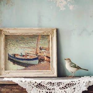 A framed painting of boats on water rests on a rustic wooden shelf with crochet lace. A small bird is perched beside it, creating a serene and artistic scene.