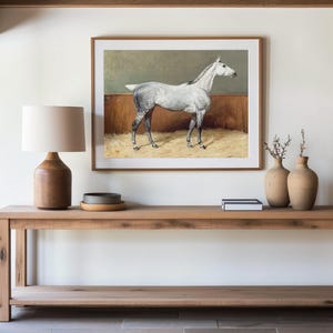 A minimalist entryway features a wooden console table with a lamp, small tray, books, and vases. A framed horse painting hangs above, creating a serene atmosphere.