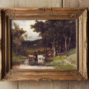 Framed painting of cows by a stream in a lush, green forest under a cloudy sky. The setting is tranquil, with rich, earthy tones and serene atmosphere.