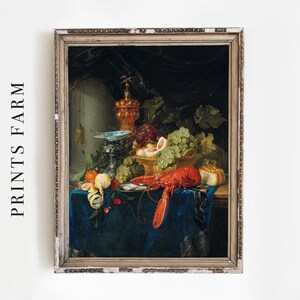 The image shows a classical still life painting featuring an arrangement of various fruits, a lobster, and decorative objects on a dark blue cloth-covered table, set against a dark background with draped fabric. The frame of the painting is ornate and weathered, adding an antique touch. The composition emphasizes richness and abundance, with grapes, peaches, and other fruits prominently displayed.