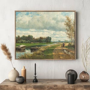 Framed landscape painting on a white wall depicts a serene countryside with a winding path, dense clouds, and two people walking. Minimalist decor below.