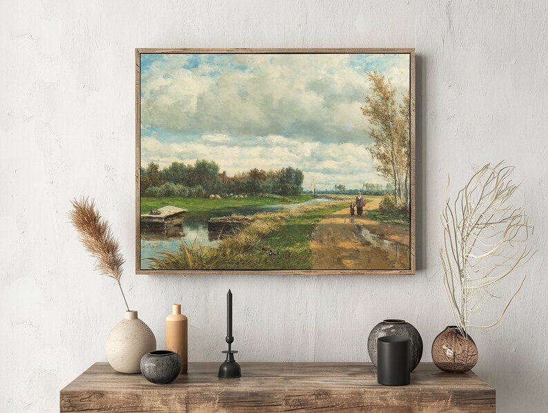Framed landscape painting on a white wall depicts a serene countryside with a winding path, dense clouds, and two people walking. Minimalist decor below.