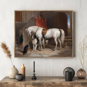 A framed painting of a white horse and two dogs next to a staircase is displayed on a wall. Vases and a candle rest on a wooden table beneath it, creating a calm, rustic atmosphere.
