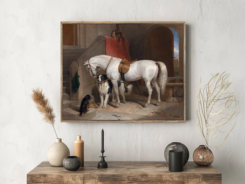 A framed painting of a white horse and two dogs next to a staircase is displayed on a wall. Vases and a candle rest on a wooden table beneath it, creating a calm, rustic atmosphere.