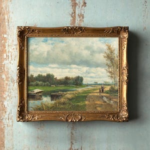 Framed landscape painting on a textured wall, depicting a serene countryside with a waterway, lush greenery, and cloudy sky, evokes tranquility.