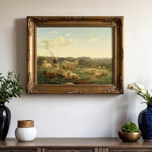 Framed pastoral painting of sheep in a green meadow on a wall. Below, a wooden console holds vases with greenery and tulips, exuding calm elegance.
