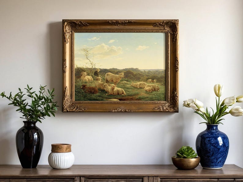 Framed pastoral painting of sheep in a green meadow on a wall. Below, a wooden console holds vases with greenery and tulips, exuding calm elegance.