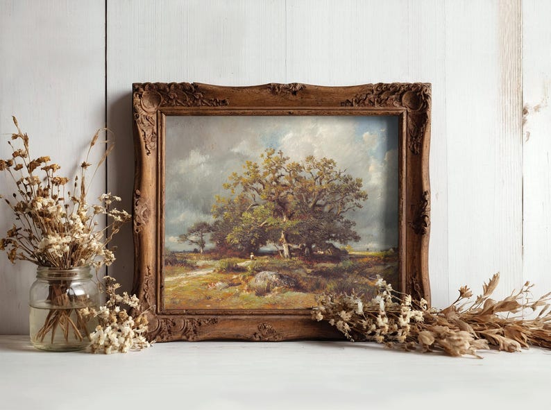 A rustic wooden frame holds a landscape painting of a tree under a cloudy sky. Dried flowers in a jar and scattered on a white surface surround it, creating a calm, nostalgic atmosphere.