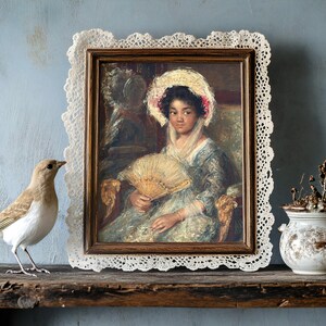 Vintage portrait of a woman with a fan in a lace-trimmed frame on a rustic shelf. A bird and a vase with dried flowers add an antique charm.
