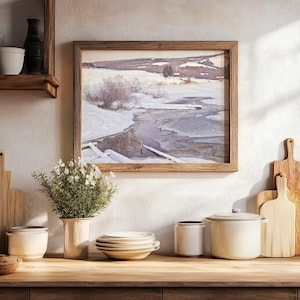 A cozy kitchen scene features a wooden shelf, stacked plates, and jars. A framed winter landscape painting hangs above a vase with flowers. Warm tones prevail.