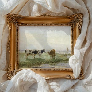 A framed painting of cows grazing in a serene countryside is set against soft, flowing white fabric. The golden frame adds a classic touch.
