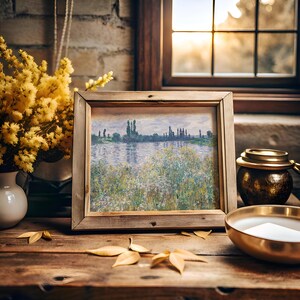 A rustic wooden table holds a framed landscape painting by a sunlit window, surrounded by golden leaves, a brass bowl, and a vase of yellow flowers.