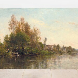 An oil painting depicting a serene landscape with a river, trees, and a soft, cloudy sky. The artwork features a palette of greens, browns, and blues, with figures near the water's edge. The painting is displayed on a white wall.