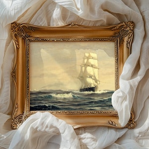 A framed painting of a tall sailing ship on the open sea, with billowing sails and waves crashing against the hull, set against a cloudy sky. The ornate, gold-colored frame surrounds the painting, which is draped with soft, white, flowing fabric.